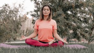 Adult woman practicing meditation on a yoga mat outdoors in a tranquil park setting.