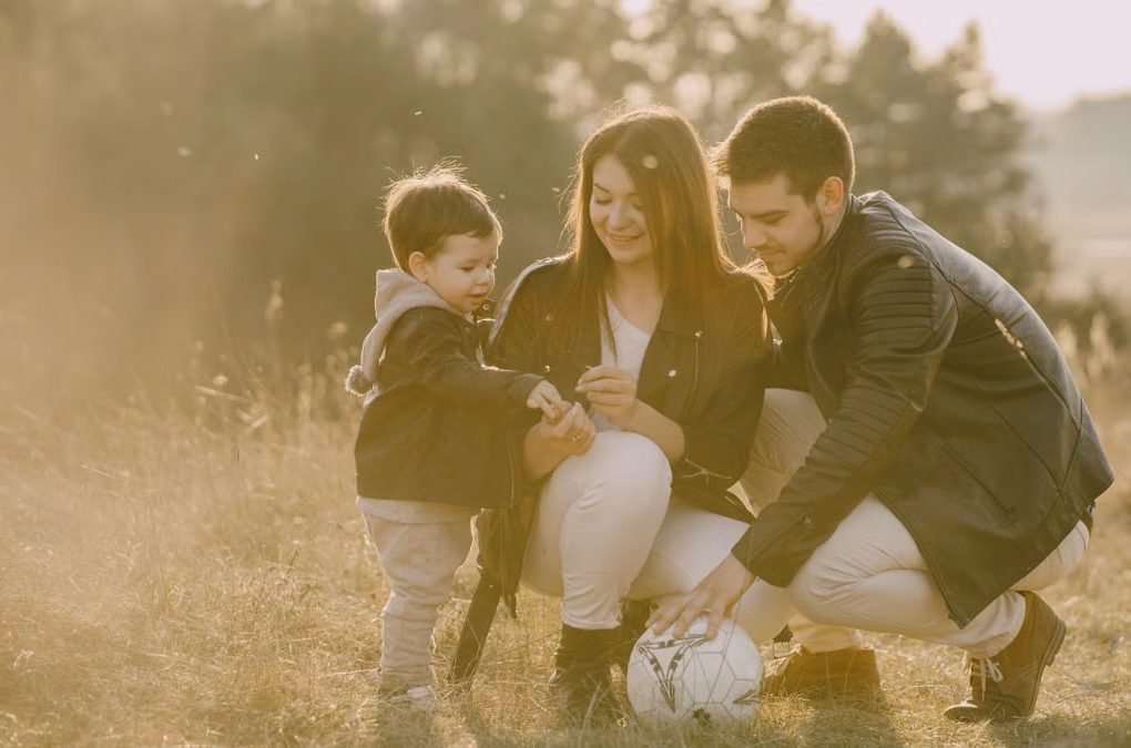 A cheerful family bonding outdoors with a soccer ball, enjoying a sunny day in the grass.