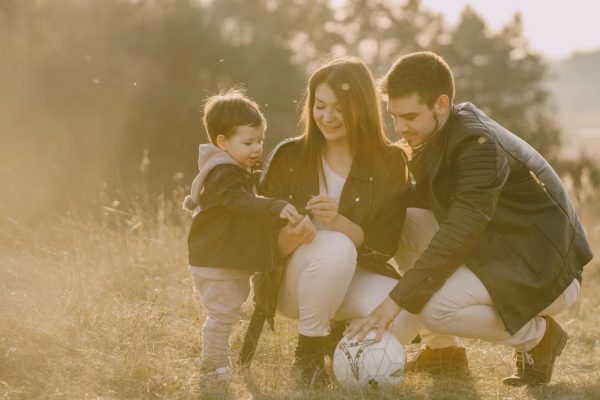 A cheerful family bonding outdoors with a soccer ball, enjoying a sunny day in the grass.