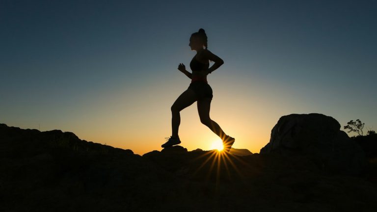 A woman runs up a trail during sunset.